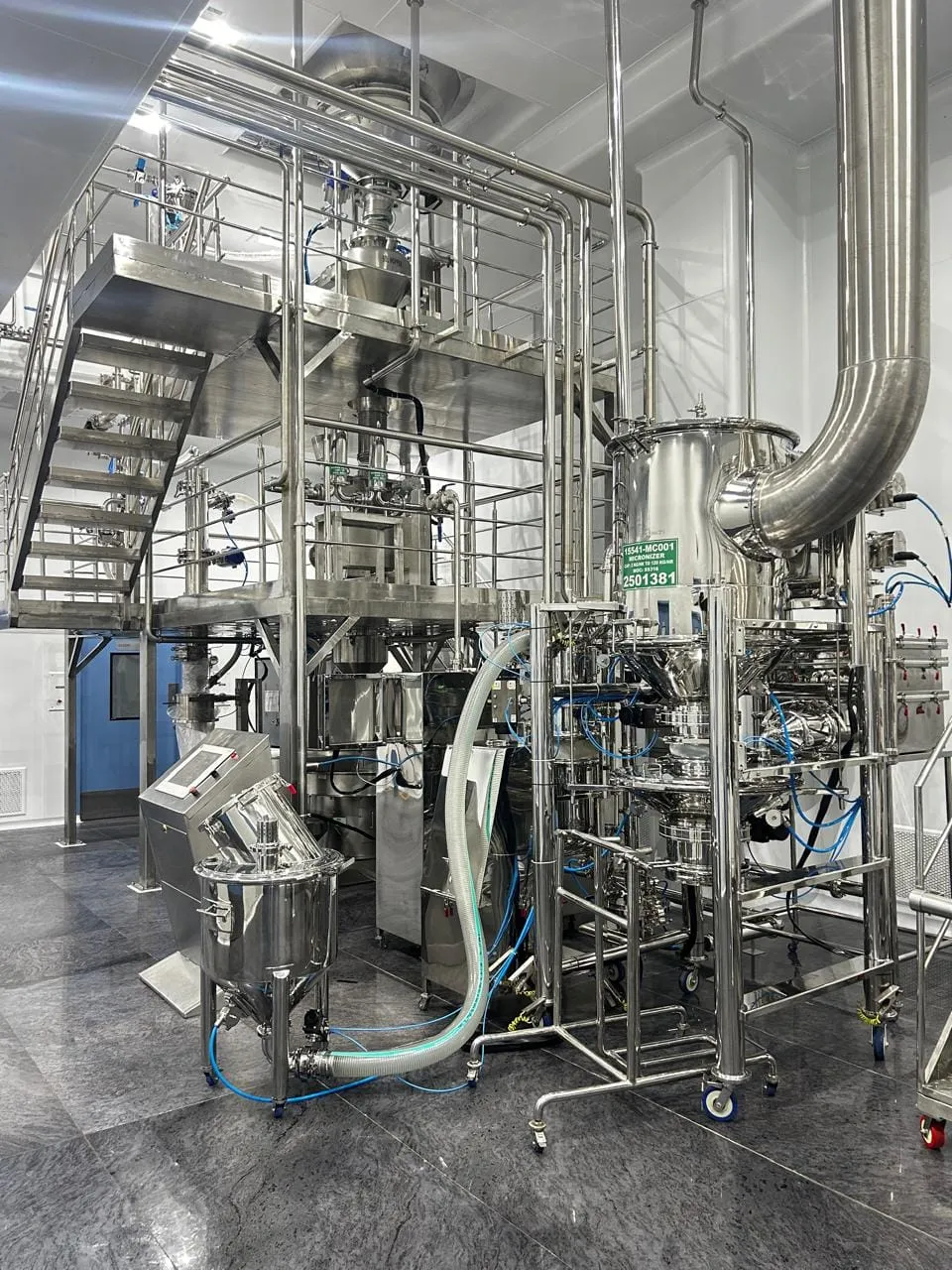 Reactor and micronizer on a stainless steel mezzanine, with transfer hoses, a charging bowl and a control panel below